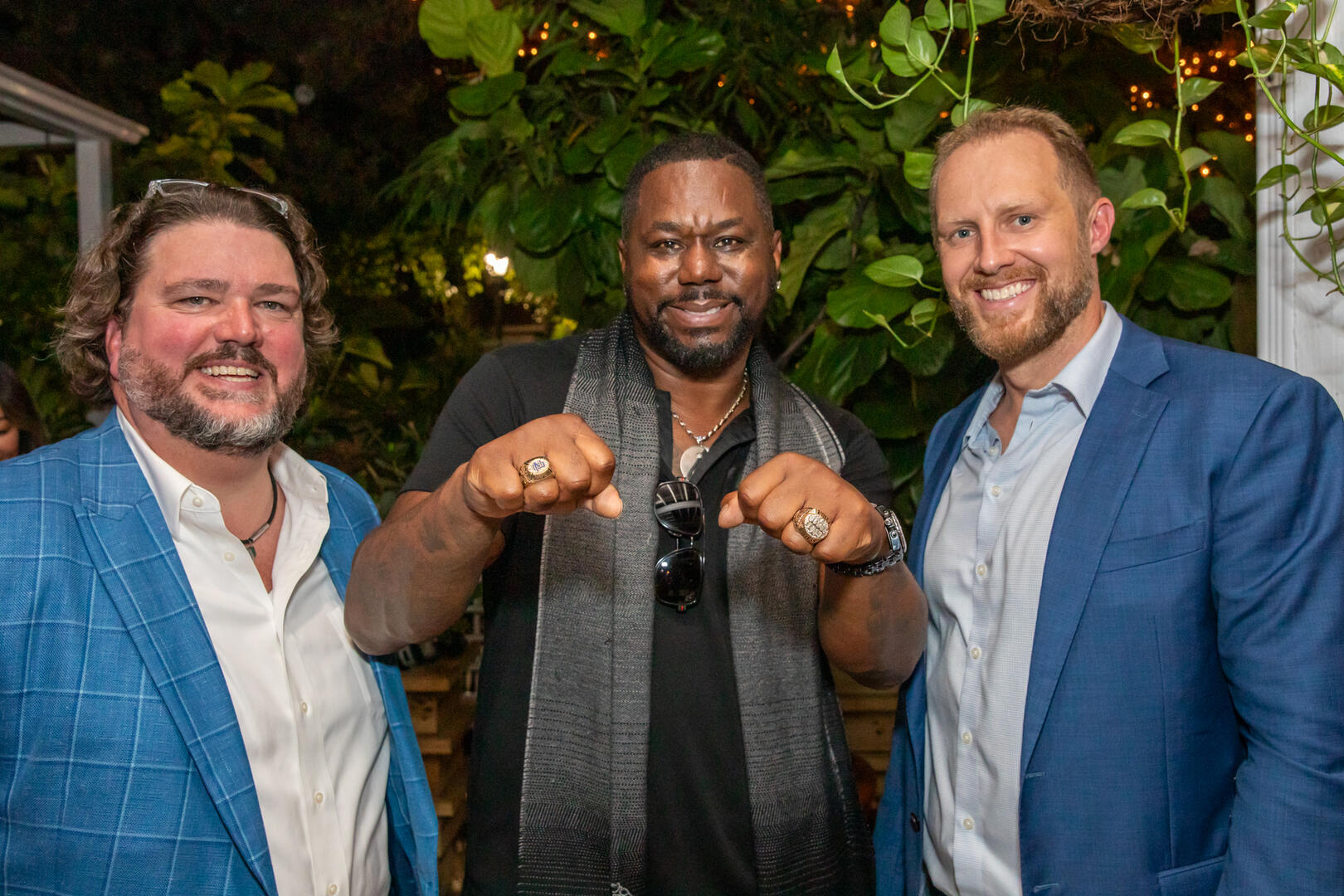 Smiling business professionals at a corporate party, with one showing off championship rings, in a vibrant New York City setting