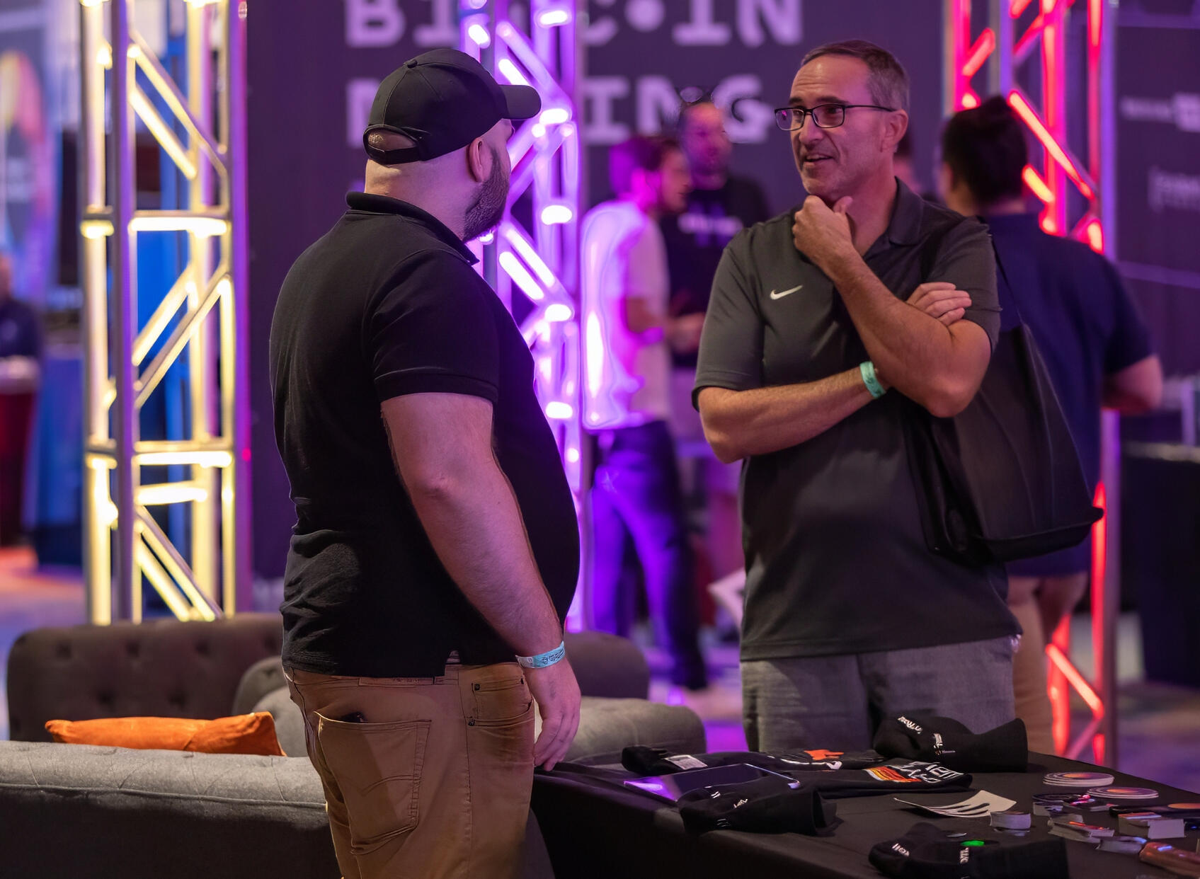 Casual discussion between attendees at a tech expo, set against colorful lighting at a NYC trade show.